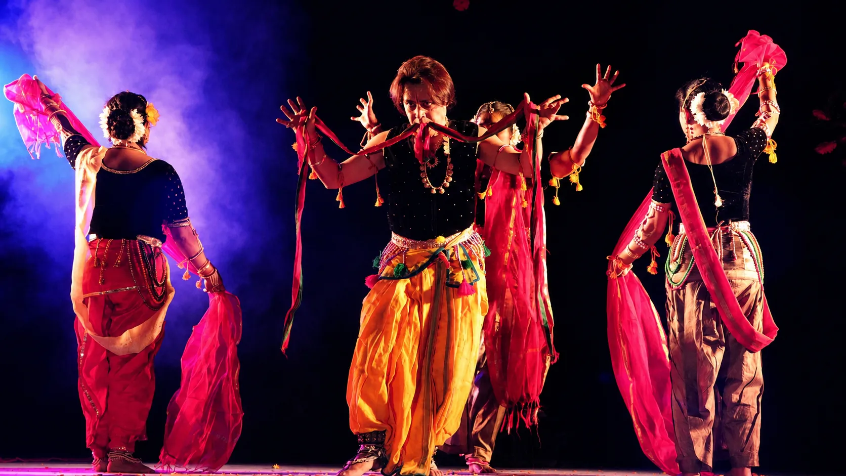 An ensemble of dancers with dupattas under warm and cool stage light