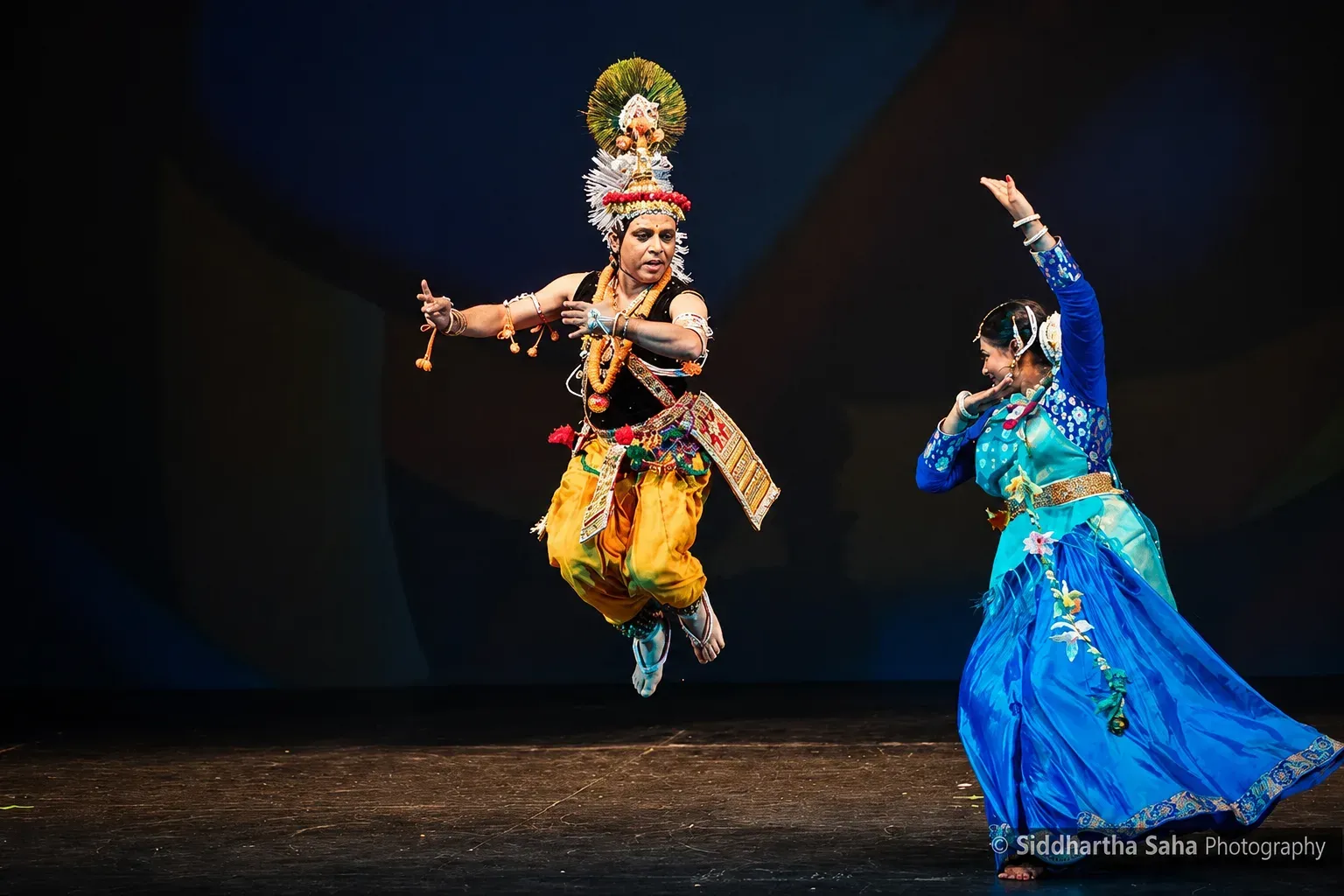 Krishna in a mid-air leap beside a dancer in blue