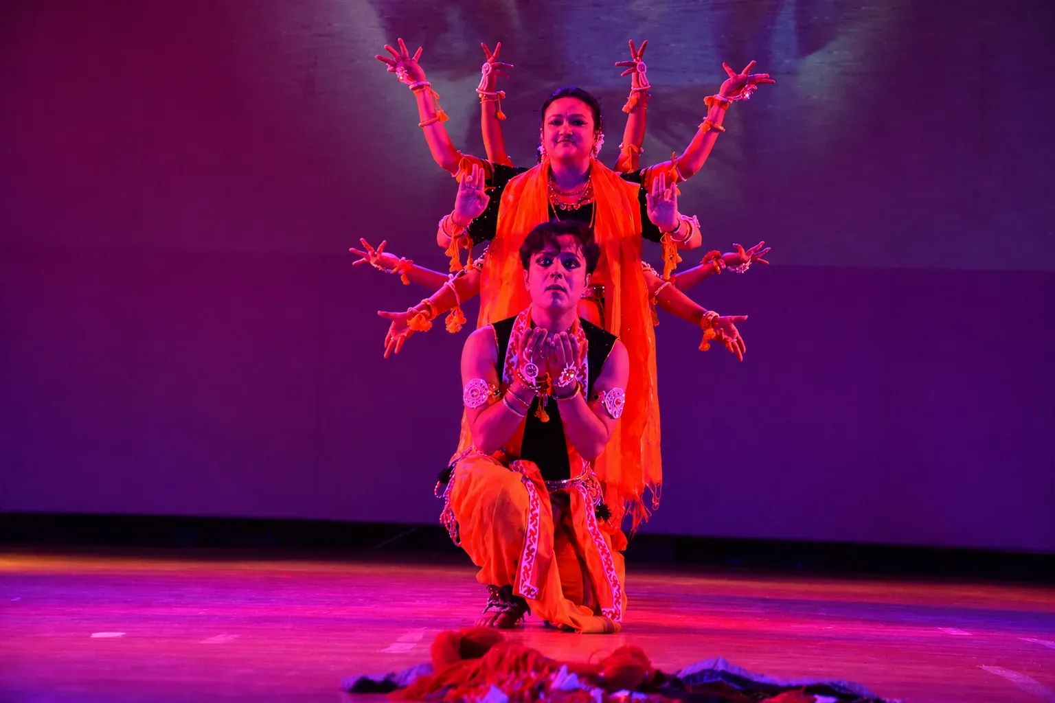 Two dancers in a multi-armed deity pose under magenta light