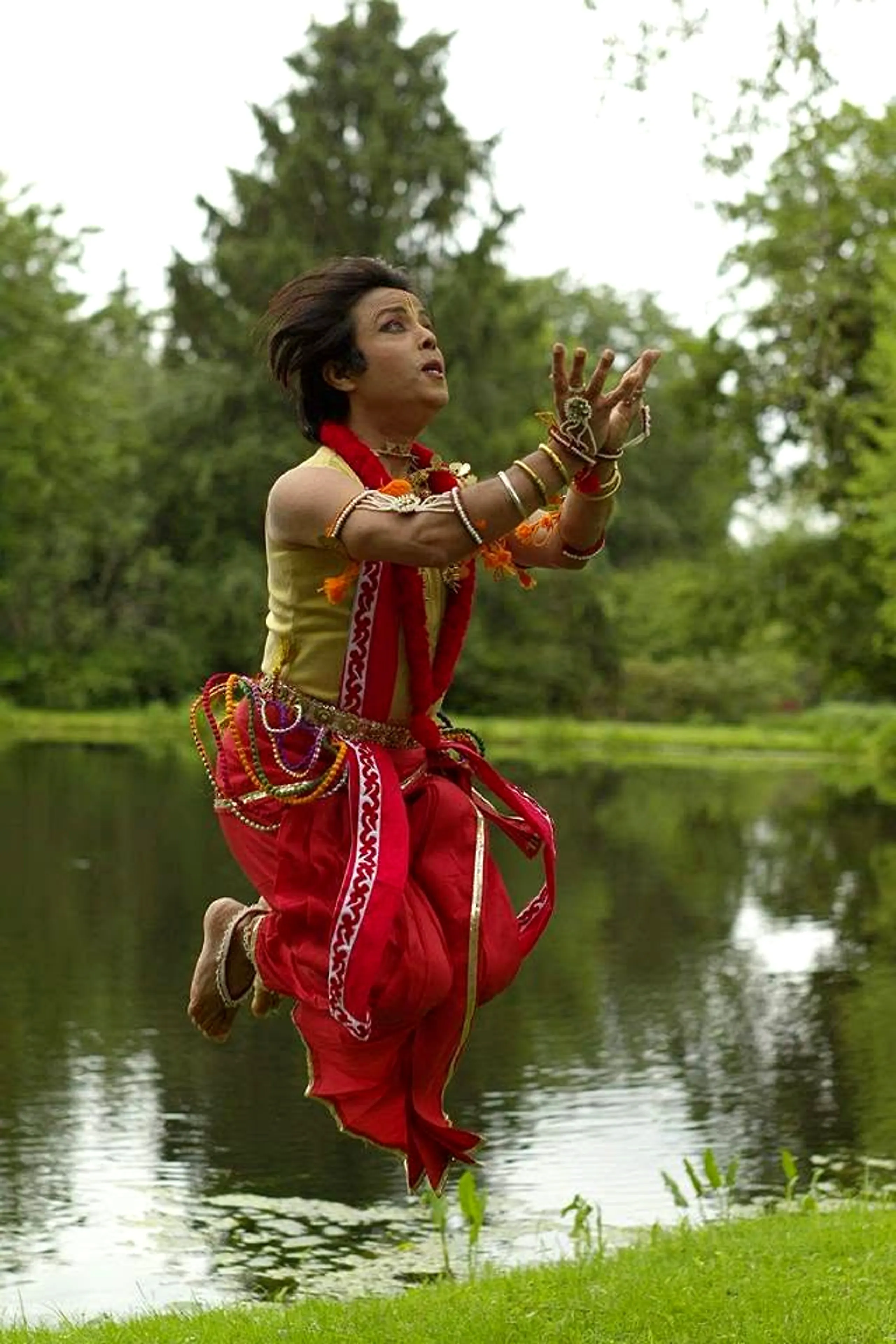 Sanjib in a mid-air leap in red costume beside a garden pond