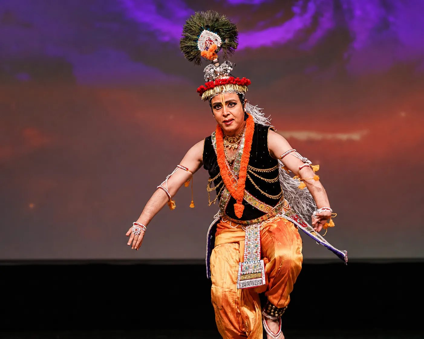 Sanjib as Krishna, crowned with peacock feathers, dancing under warm light